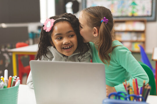 Schoolgirl whispers secret, making friend laugh in class.