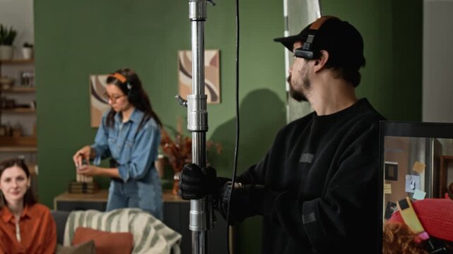 Caucasian male gaffer adjusting lighting C-stand on studio set while film crew prepares for shooting. Footage suitable for commercial video production, backstage projects and media training