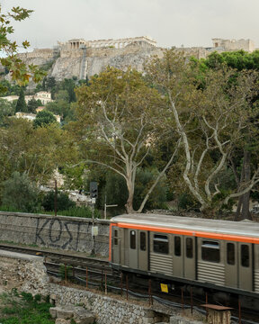 Graffiti covered metro train below the Acropolis in Athens, highlighting the contrast between ancient heritage and modern urban life.