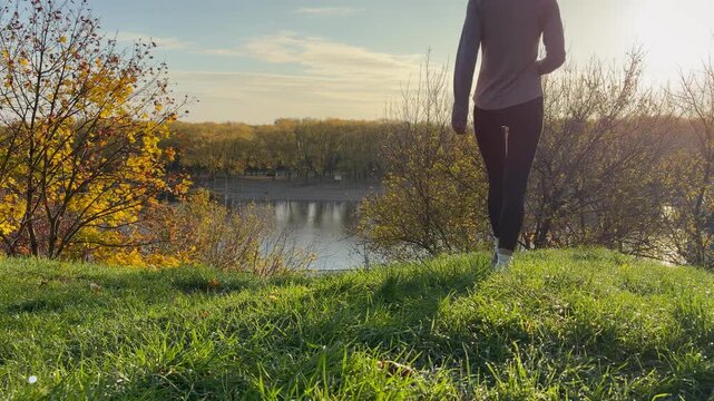 A woman in sportswear walking and jogging up a dewy grassy hill in the bright morning sun. Fitness, healthy lifestyle, morning routines, and outdoor exercise.