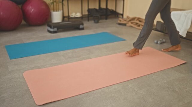 Woman sits cross legged on a pink yoga mat, bare midriff visible, holding a small timer and settling into posture in studio; mindful calm.