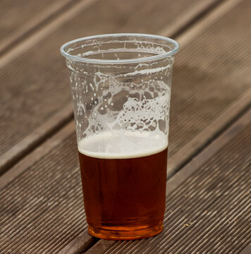 Half-full plastic cup holds amber beer with white foam
