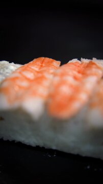 Hands placing shrimp on top of a sushi roll, ebi roll preparation close-up, vertical video