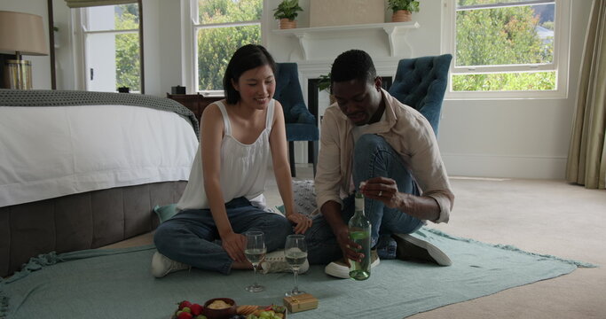Couple sitting on bedroom floor, pouring wine and sharing joyful conversation