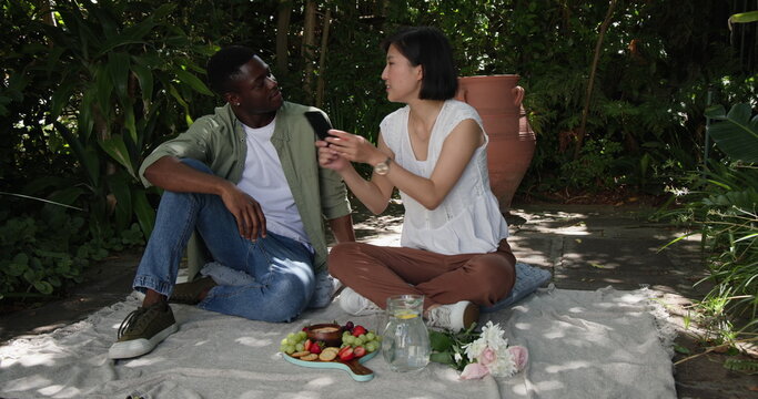 Couple enjoying picnic on blanket, sharing fruits and conversation in garden