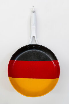 A pan painted with the national flag of Germany (black, red, yellow) hanging on a white wall. 