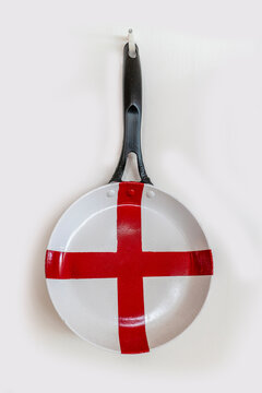 A pan painted with the national flag of England (red cross on white background) hanging on a white wall. 