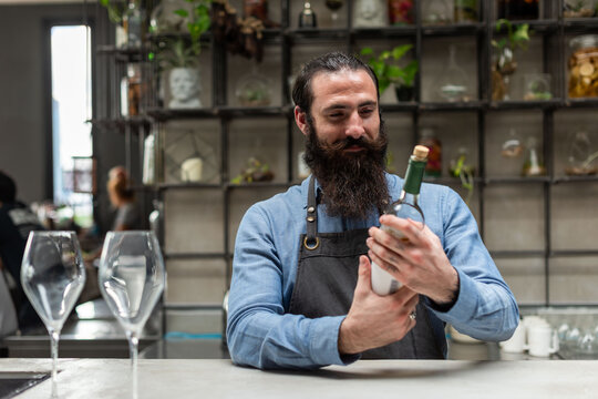 Bearded bartender examining wine bottle
