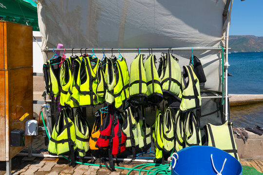 Row of vibrant yellow and red life jackets hanging on a rack at a seaside water sports rental station. Conceptual photo representing water safety, lifeguard equipment, summer vacation