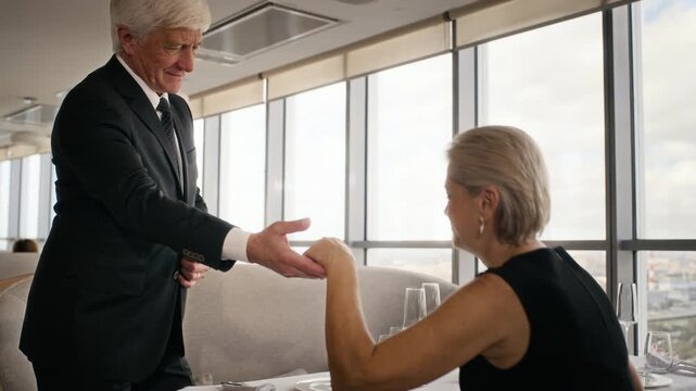 Senior Caucasian couple taking seats at restaurant table while waiter presenting menu. Footage suitable for fine dining marketing, luxury lifestyle campaigns and hospitality commercials