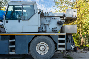Side view of a large wheeled mobile crane showing its operator cabin, telescopic boom base, heavy-duty tire, hydraulic components and stabilizing outrigger. Industrial lifting vehicle used for constru © Volha