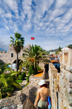 Woman with sun hat walking on ancient Marmaris castle walls with Turkish flag and palm trees, Mugla, Turkey