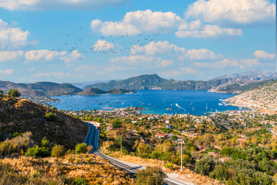Aerial view of Selimiye bay with boats, coastal road and birds flying in blue sky, Marmaris, Mugla, Turkey