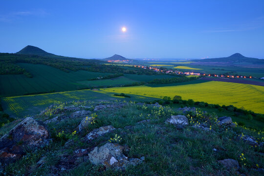 Full moon glowing over volcanic peaks and illuminated villages during blue hour