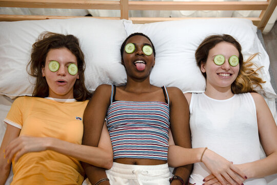 Three women relaxing with cucumber slices on their eyes, smiling.