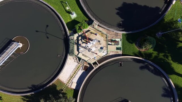 Modern wastewater treatment plant with three large circular clarifier tanks surrounded by green lawns and solar panels, seen from above
