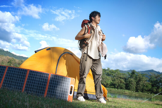 Adventurous traveler with a backpack on their shoulders is setting off, while a solar panel sits beside a yellow tent, soaking up sunlight to generate electricity.