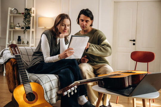 Couple reviewing sheet music together beside acoustic guitar and stringed instrument in a warmly furnished home interior, candid domestic scene