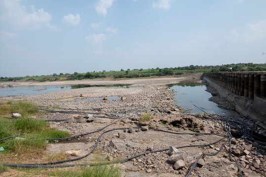 A dry river area during the prolonged dry season, showing severely reduced water levels and exposed riverbanks. The surrounding soil has dried, hardened,