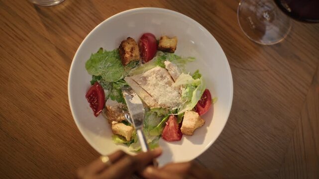 POV of African American woman cutting chicken Caesar salad with fork and knife during restaurant dinner. Clip suitable for healthy eating campaigns and hospitality advertising