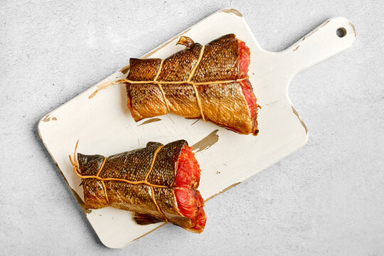 Hot smoked salmon wrapped and tied with string placed on cutting board. Scene shows food preparation in kitchen.