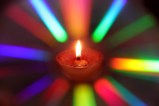 A burning diya (oil lamp) surrounded by colorful rainbow-like light streaks created using light diffraction 