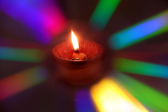 A burning diya (oil lamp) surrounded by colorful rainbow-like light streaks created using light diffraction 