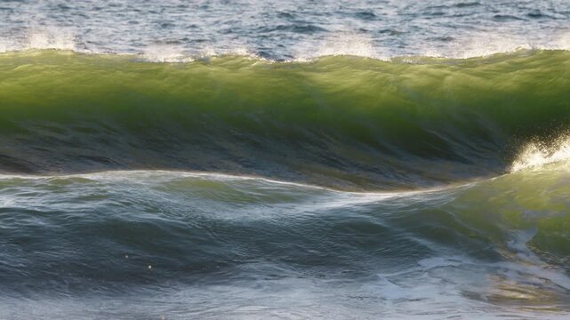 Storm wave crashing in ocean with evening warm sunlight