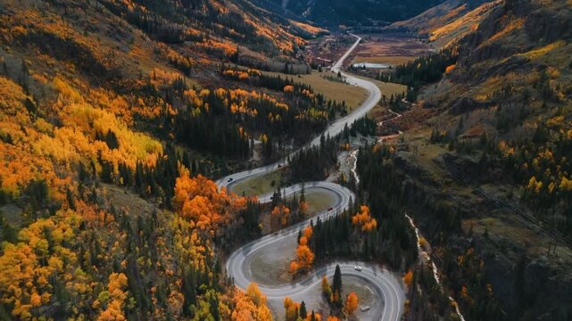 Aerial View of a Winding Mountain Road with Cars Driving Through a Deep Valley Forest 