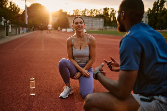 Athletes rest and talk during running training on an outdoor track at sunset