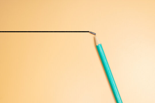 Green pencil with a broken graphite tip on a peach background with copy space, illustrating mistakes, setbacks and interrupted creativity.