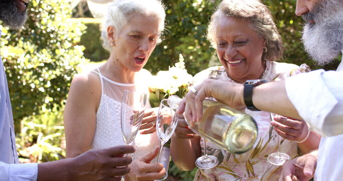 Pouring wine into glasses, senior friends enjoying outdoor wedding together