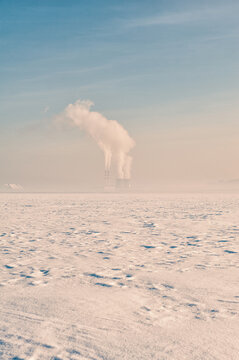Frozen winter snow field landscape. Industrial factory plant smoke pollution