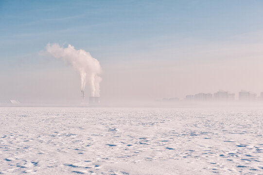Frozen winter snow field landscape. Industrial factory plant smoke pollution