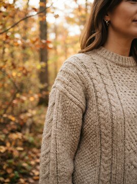 Woman wearing a cozy cable knit sweater in an autumn forest.