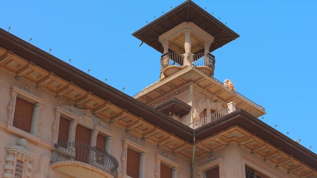 Ornate villa tower and sculpted facade with shuttered windows, curved balconies and blue sky