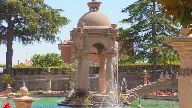 Domed garden pavilion on sculpted columns surrounded by fountain jets, trees and an ornate bridge
