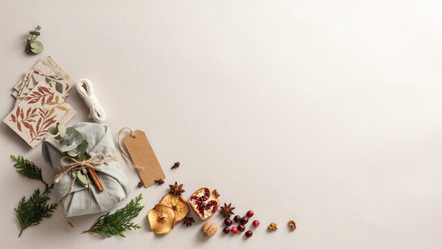 Rustic Christmas Present Wrapped in Sage Green Linen with Jute Twine, Eucalyptus and Cinnamon, Surrounded by Dried Fruit, Evergreen Sprigs and Recycled Craft Paper