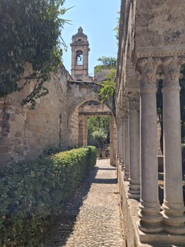 Prospettiva del chiostro di San Giovanni degli Eremiti con antiche arcate in pietra e campanile che emerge sullo sfondo nel centro storico di Palermo.