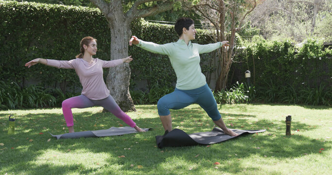 Happy caucasian lesbian couple practising yoga in sunny garden, slow motion
