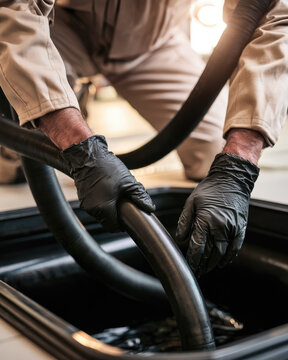 Grease trap waste suction service technician guiding flexible hose into commercial kitchen interceptor during facility maintenance
