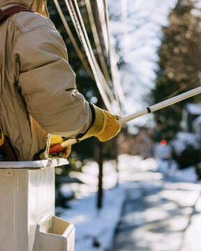 Utility lineman wearing insulated parka and gloves in aerial bucket lift during snowy power line maintenance