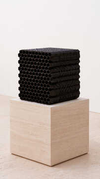 Black structured filter media on travertine pedestal with repeating hexagonal channels, minimalist environmental technology study, crisp texture and ample neutral space for design use