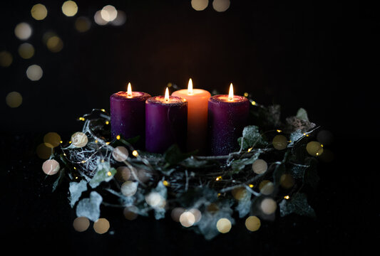 Four burning Advent candles in Christmas wreath during holiday season.