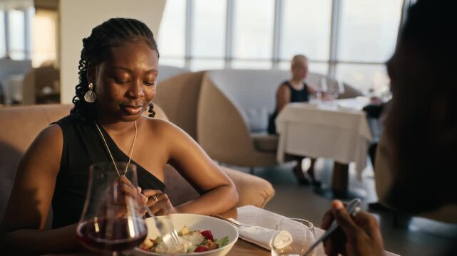 African American young adult couple eating fresh salads and talking during luxury restaurant date. Footage suitable for fine dining advertising, dating campaigns and hospitality commercials