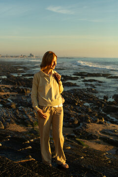 Woman standing on a rocky seashore and looking toward the ocean in warm golden evening light