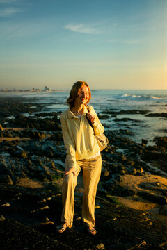Woman standing on a rocky seashore with her eyes closed in warm golden evening light