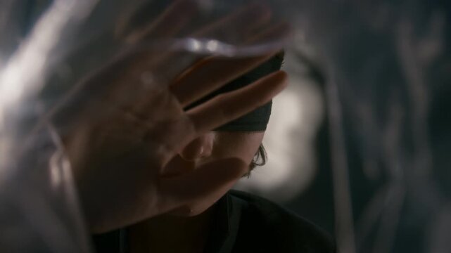 Blindfolded Caucasian young woman touching transparent plastic film with hands in close up shot. Clip suits mental wellbeing projects exploring psychological barriers or sensory perception