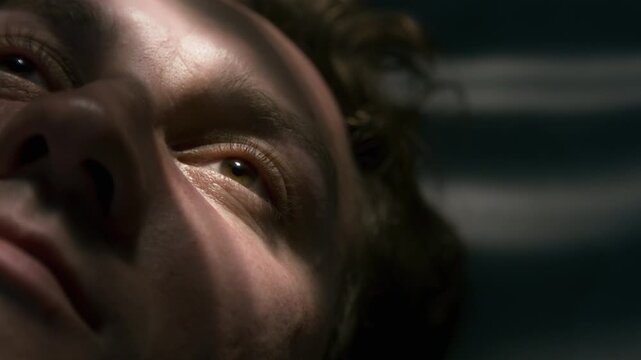 Caucasian young adult man lying down, opening eyes and blinking in extreme close up. Ideal for sleep disorder awareness, mental health campaigns, and morning wellness advertising