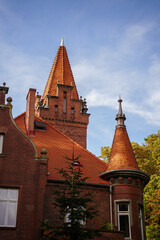 Gothic revival castle turret featuring intricate red brickwork and terracotta tiling against a blue sky, showcasing historical European architecture, historical architecture, Gdansk, Poland © Olga Yashnikova